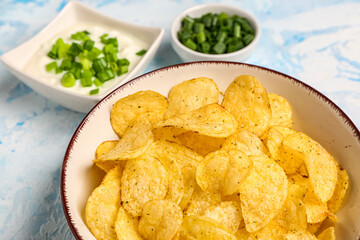 Bowls of tasty sour cream with sliced green onion and potato chips on blue background