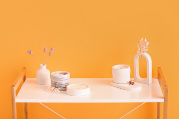 Holders with candles and decor on table near orange wall in room