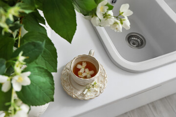 Cup of tea with jasmine flowers on white kitchen counter, closeup