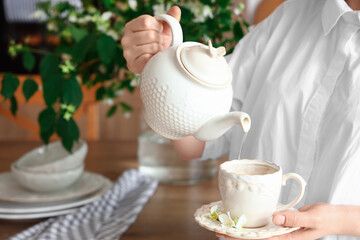 Woman preparing tea with jasmine flowers in kitchen, closeup
