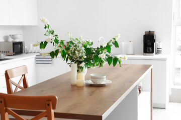Vase with blooming jasmine flowers, candles and bowls on wooden table in modern kitchen
