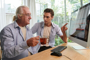 Young man helping grandfather to book flight online