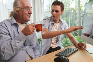 Cheerful young man showing grandfather how to buy plain ticket online