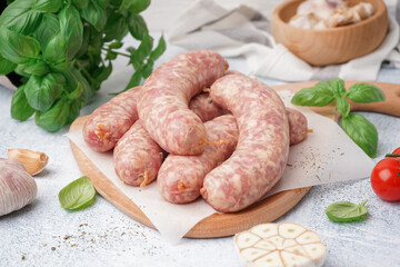 Wooden board with raw homemade sausages on light background