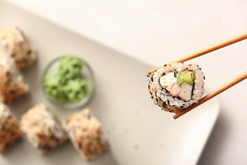 Chopsticks with tasty sushi roll on light background