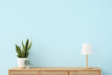 Modern chest of drawers with houseplants and lamp near blue wall in room