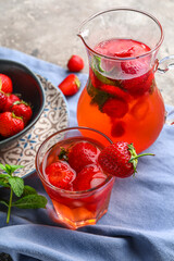 Glass and jug of infused water with strawberry on grunge background