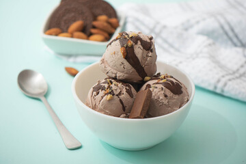 Chocolate ice cream decorated with nuts and chocolate icing, in a white bowl, blue background. Summer homemade cooling desserts