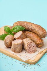 Wooden board with tasty homemade sausages on blue background