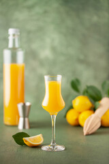 Limoncello in grappas wineglass, sweet Italian lemon liqueur, traditional strong alcoholic drink and lemons on the green wooden background.