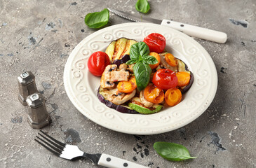 Plate with grilled vegetables and basil on grey background