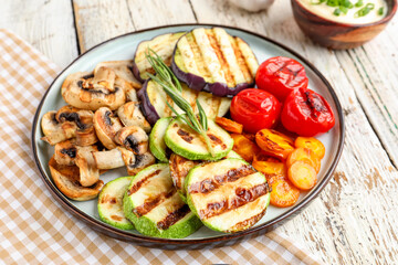 Plate with grilled vegetables and sour cream on white wooden background