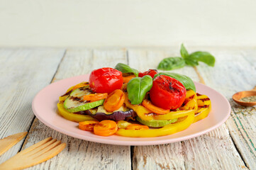 Plate with grilled vegetables and basil on white wooden table