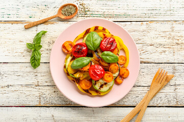 Plate with grilled vegetables and basil on white wooden table