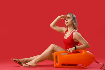 Female lifeguard with rescue buoy sitting on red background - Powered by Adobe