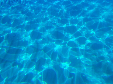 Dark blue ocean surface seen from underwater. Abstract waves underwater and rays of sunlight shining through, Sun light rays undersea deep, Underwater background with sea bottom, Mediterranean sea