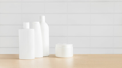 A set of cosmetic bottles and creams against a white wall.