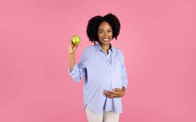 Smiling millennial african american curly pregnant lady in casual with big belly show green apple