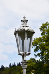 A white lantern with a lot of beautiful elements located in a park on the background of a blue sky and green trees