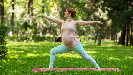 Pregnant caucasian woman doing yoga in the park. Warrior Pose. 