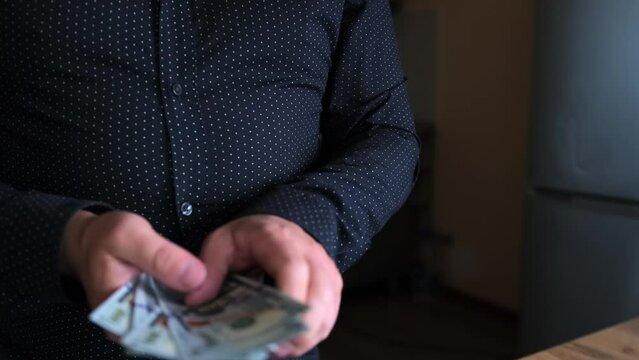 Businessman in a dark shirt taking profit from the transaction in cash US dollars. Concept of financial wealth, money, and power.