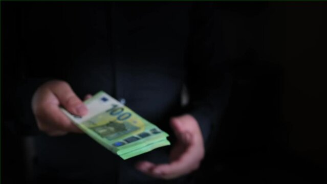 Businessman in dark shirt taking profit from the transaction in cash banknotes of 100 euros, close up. Concept of financial wealth, money, and power.