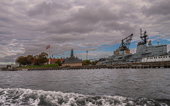 Copenhagen, Denmark - September 14, 2010: East shore harbor. Military domain and marine, navy, museum with Peder Skram frigate under gray cloudscape. Danish flag near royal building