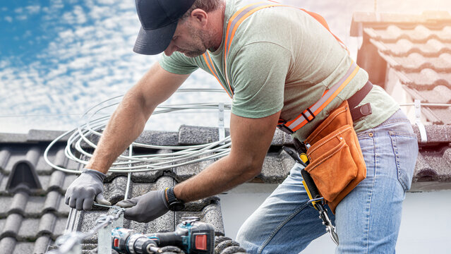 Work on the roof. An electrician`s hands turning screw using a spanner during installing a lightning rod conductor on a tiles roof.