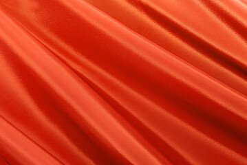 Texture of a smooth luxurious, elegant fabric in orange, red. Purple satin or silk fabric with folds and waves