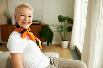 Horizontal closeup image of cheerful lady of 60s in casual trendy clothes and silk scarf around...