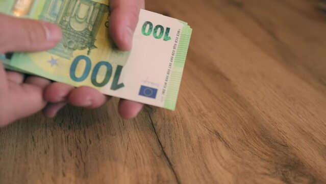 Close up, man's hand folds pack of 100 euro bills in cash and holding out wad of money. Bribery and extortion of money concept.