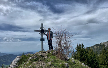 Bergwanderer (männlich) am Gipfelkreuz des Schweinsberg, Bayern, Deutschland, Alpen