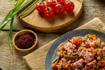 Israeli couscous with sumac and pieces of stewed chicken on a table on a linen napkin in a plate next to spices and vegetables
