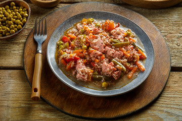 Israeli couscous with sumac chicken pieces and vegetables in a plate on a wooden round stand next to a fork.