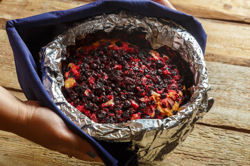 An open pie with blueberries freshly baked in foil in female hands a blue towel.