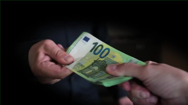 People are trying to divide money among themselves in dark room, man's hand is pulling pack of 100 euro bills strongly, close up, black vignette.