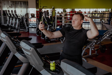 Man in the gym takes selfie and shows his muscles and biceps