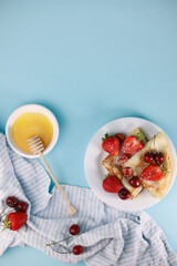 delicious fragrant pancakes folded in a triangle on a white plate and a blue background and decorated with delicious ripe sweet strawberries, red fragrant cherries and coconut flakes