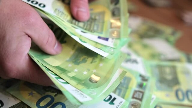 Close up, man counting hundred euro bills in cash and pass it to woman's hand, table with pile of euro banknotes on background revolve. Financial management and budgeting.