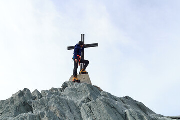 Mountaineer man standing at summit cross of mountain Allalinhorn in Pennine Alps, Switzerland