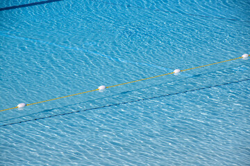 A image of the rippling pool surface from above. There is a yellow pool line in the pool. Scenic and tranquil summer vacation, water reflection.