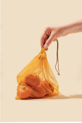 Reusable bags for buying vegetables and fruits. A woman's hand holds bags with tomatoes.