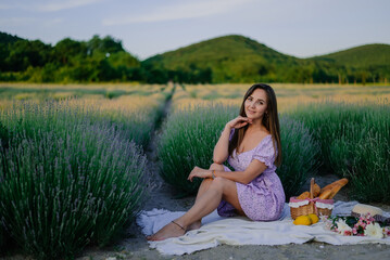 close-up portrait of a young beautiful woman in summer on a lavender field at a picnic with a basket of fruits, a baguette, a croissant