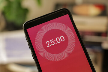 A phone with a red and white 25-minute timer to study with the pomodoro method on a blurry background. Perfect for students planning their time studying, doing homework, being productive.