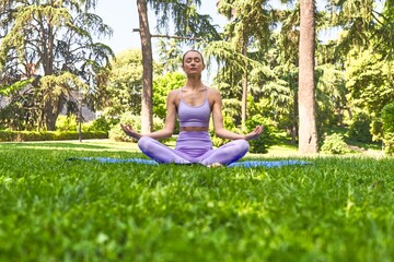 Doing yoga stretches on a mat, a woman in sportswear enjoys a tranquil park morning.