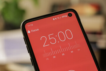 A phone with a red and white 25-minute timer to study with the pomodoro method on a blurry background. Perfect for students planning their time studying, doing homework, being productive.