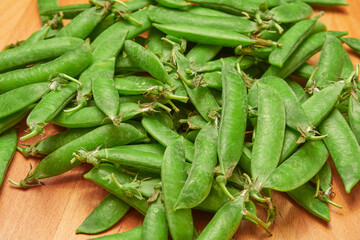 green ripe plucked pea pods on a wooden kitchen cutting board close-up
