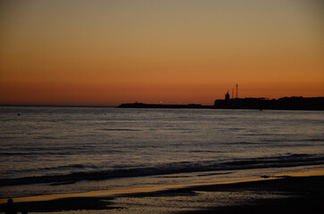 Colorful sky at sunset on the coast of Conil in Spain, looking at the lighthouse on the rocky coastline