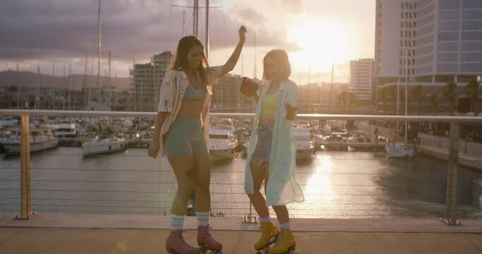 Two best friends dancing and sliding on rollerblades at sunset. Free spirits, experiencing freedom and youth. Young women have fun with instant vintage camera. Funky sport or fitness outdoors.