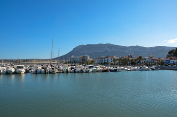 Fototapeta na wymiar View of a pier of the yacht and sailing port of Denia with houses on the promenade and the mountainous coast in the background